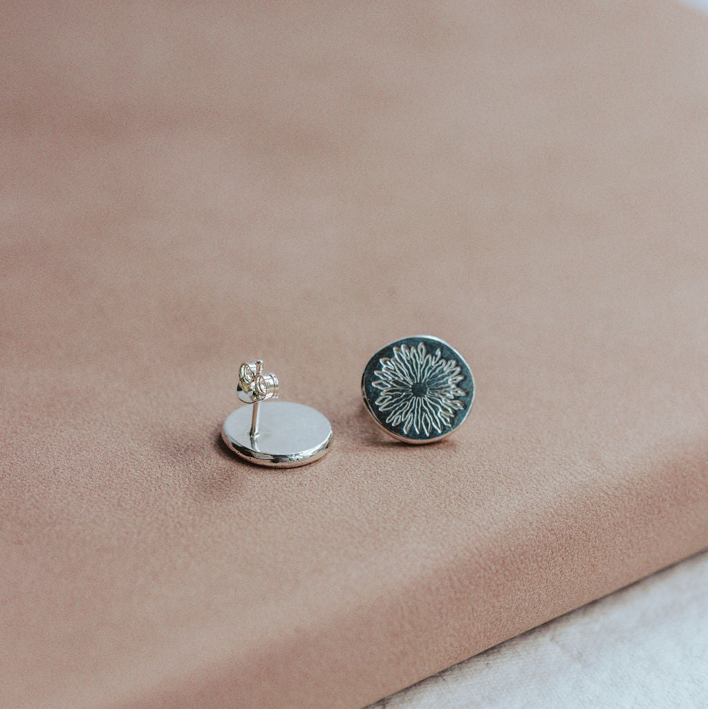 Pair of silver earrings with sunrise design on a beige surface