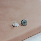 Pair of silver earrings with sunrise design on a beige surface