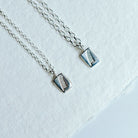 Two feather charm pendants on a white background. One with a slightly chunkier chain than the other.