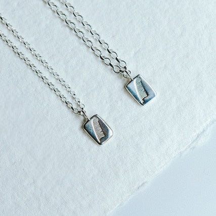 Two feather charm pendants on a white background. One with a slightly chunkier chain than the other.