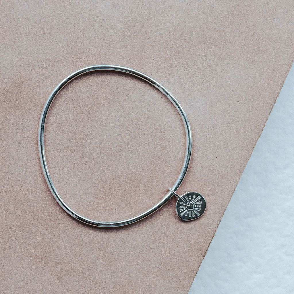 Silver bangle with a heart design on a beige background