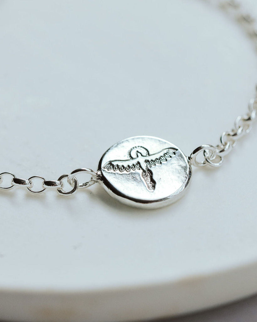 Silver bracelet with a phoenix charm on a white plate