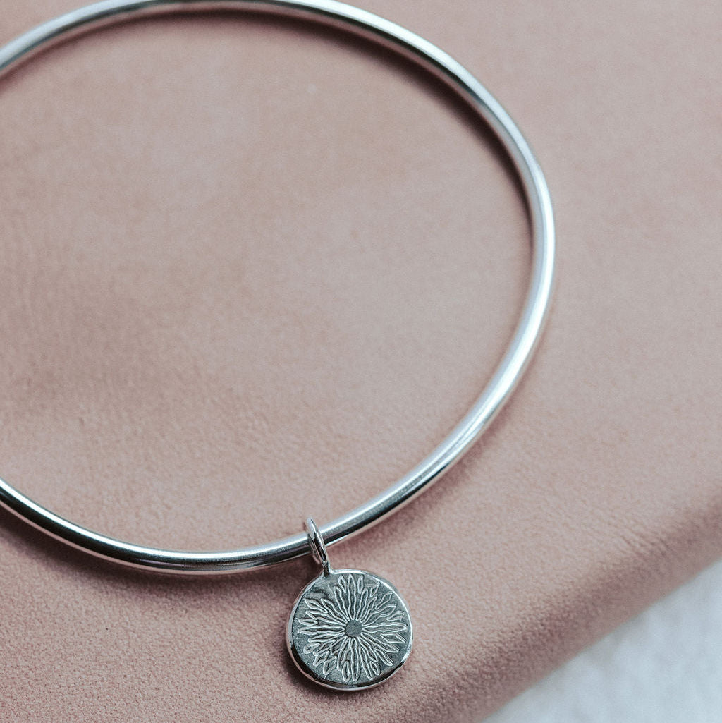 Silver bangle with a round sunrise pendant on a pink surface