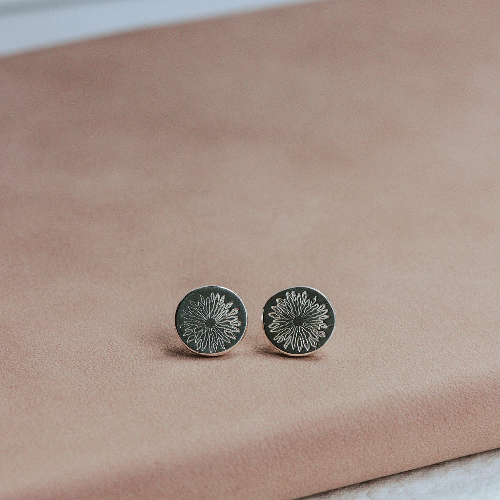 Pair of silver sunrise stud earrings on a pink surface