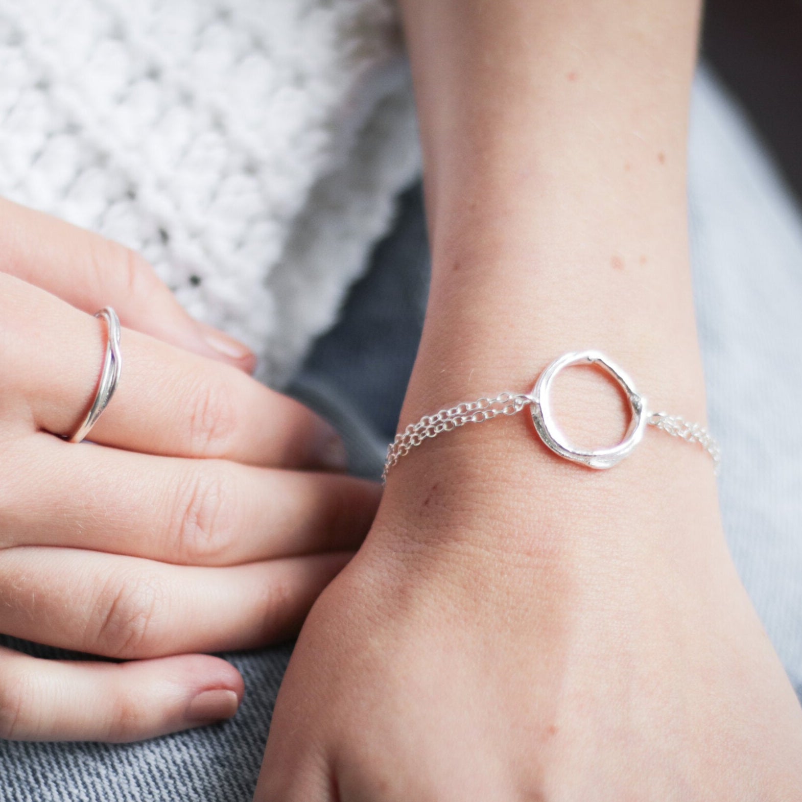 Close-up of hands wearing silver ring and bracelet on a blurred background