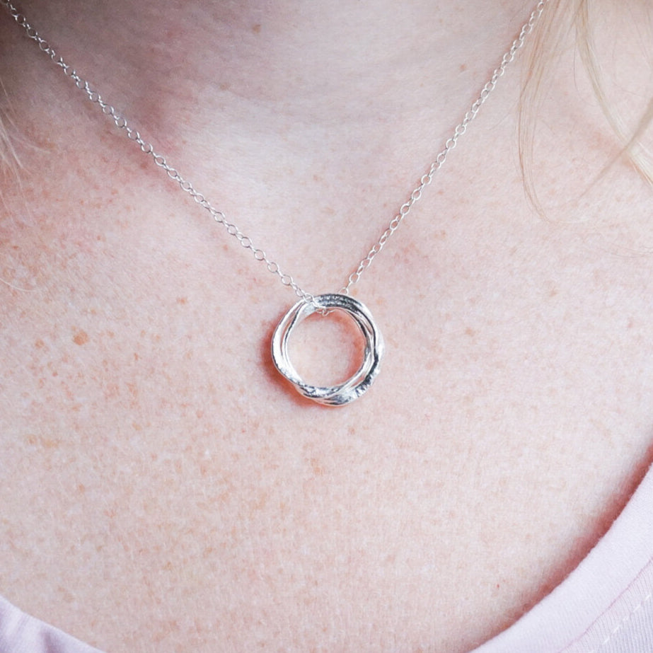 Silver necklace with a interlocking circles pendant on a person wearing a white shirt.